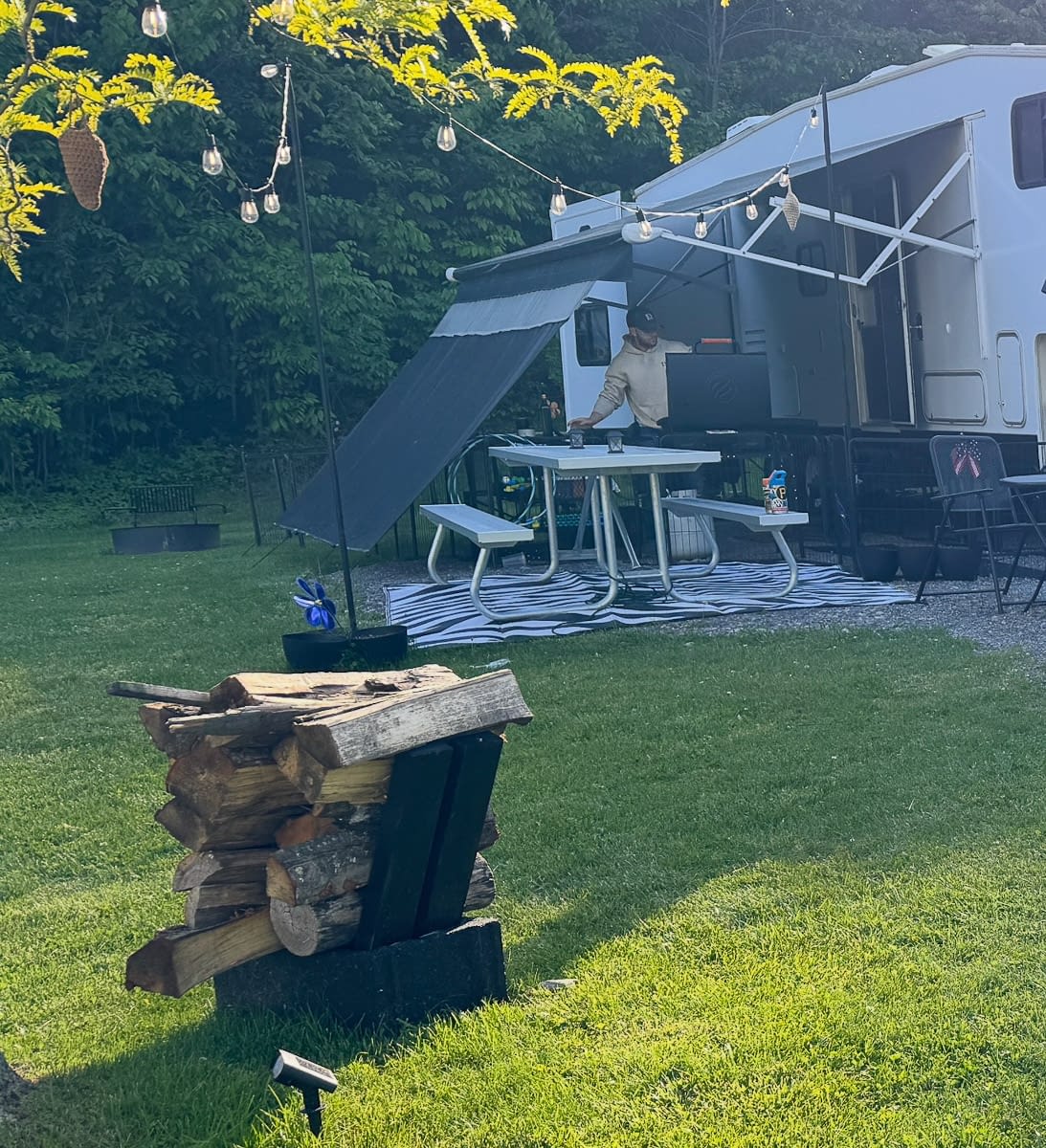 Cozy RV outdoor setup ideas with awning shade, string lights, firewood holder, and campsite seating.