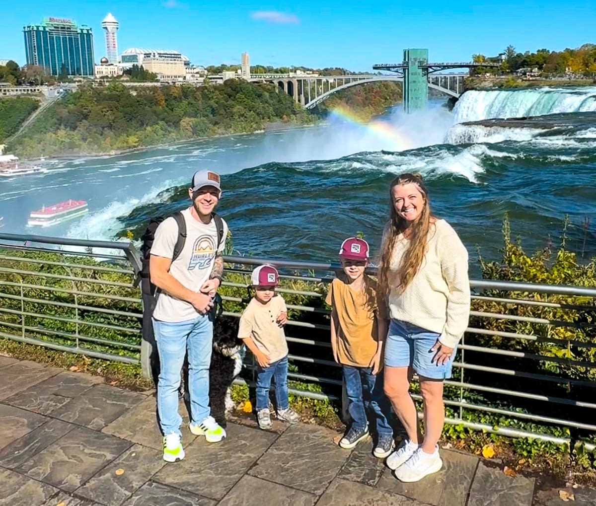 Family visiting Niagara Falls with Canada, the falls, a rainbow, and the Maid of the Mist boat in the background.